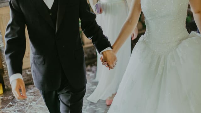 A romantic moment capturing a bride and groom holding hands in elegant wedding attire indoors.