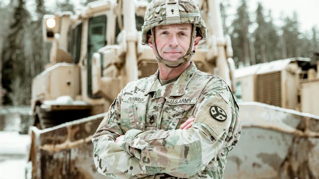 Military engineer in uniform standing confidently beside a snow-covered bulldozer.