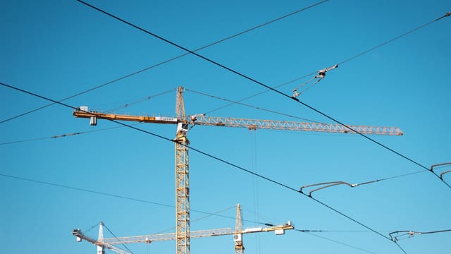 Tower cranes stand tall with intersecting power lines under a clear blue sky.