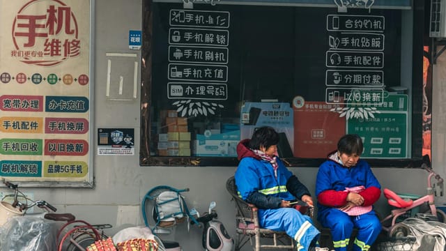 Two workers in blue uniforms rest outside a mobile repair shop with signage.