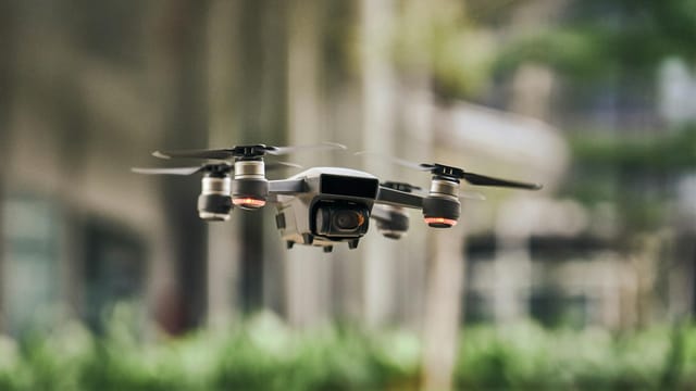 Close-up of a modern quadcopter drone hovering outdoors with blurred greenery background.