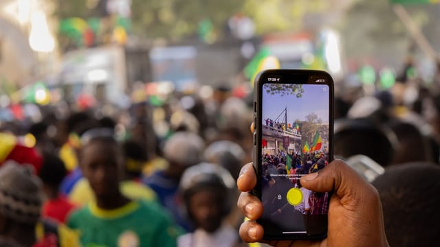 A lively street scene in Senegal with people celebrating, viewed through a smartphone screen.
