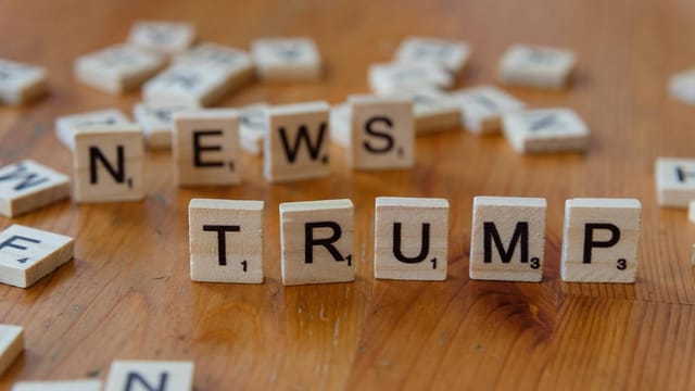 Wooden letter tiles spell 'NEWS' and 'TRUMP' on a wooden table, relating to political discourse.
