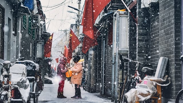 Two people in a snowy alley with red flags, capturing a peaceful winter moment.