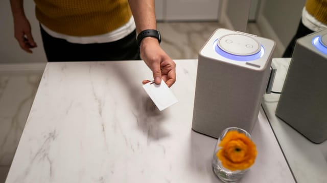 A person interacts with a smart speaker on a marble table, showcasing contemporary technology use.