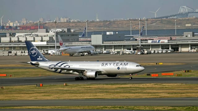 SkyTeam aircraft taxiing on a runway with a bustling airport backdrop.