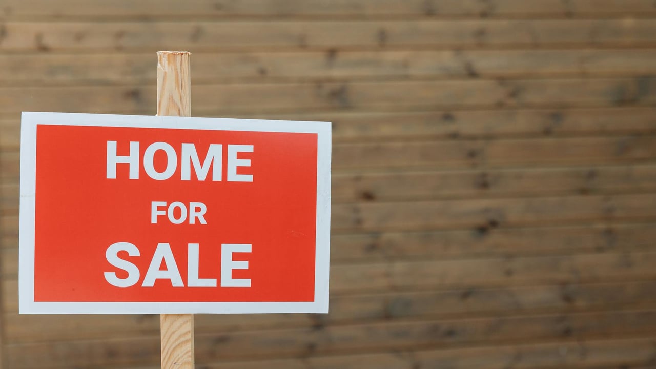 Close-up of a red home for sale sign against a wooden backdrop, ideal for real estate use.