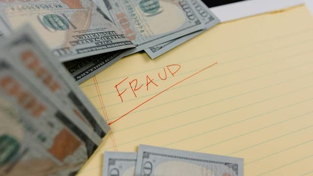 Close-up of US dollars and 'Fraud' written on yellow paper, representing financial scams.