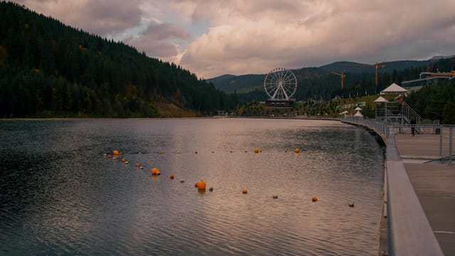 Tranquil lakeside view surrounded by mountains with a prominent Ferris wheel. Ideal for travel imagery.