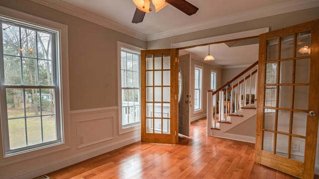 Spacious living room with wooden French doors and ceiling fan, showcasing contemporary interior design.