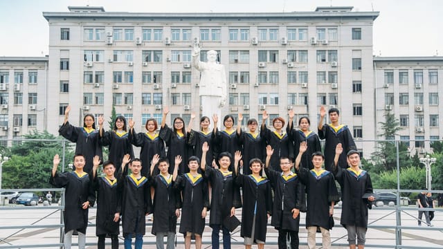 Group of graduates in gowns posing outdoors in front of university building.