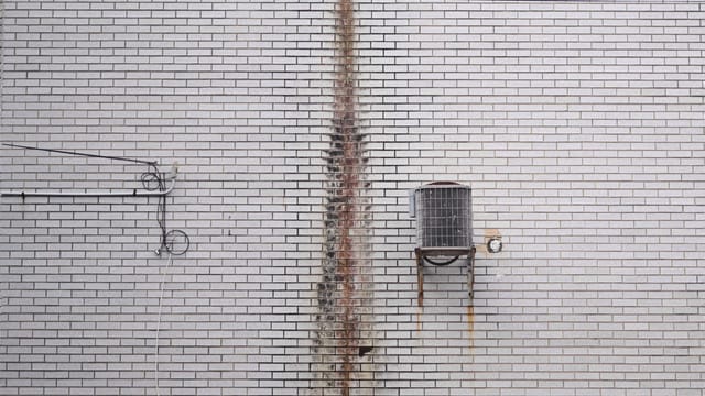 Close-up of a rusted air conditioning unit on a white brick wall for industrial themes.