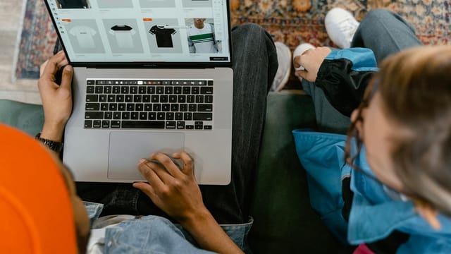 Two people browsing online clothing store on a laptop from above.