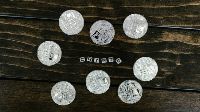 Silver cryptocurrency coins arranged on a wooden surface spelling 'crypto'.
