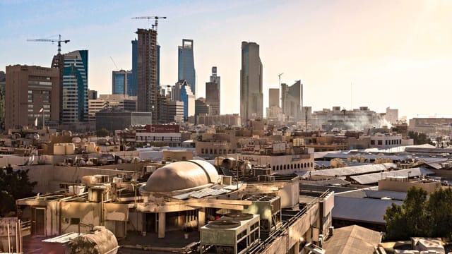 Skyline of Riyadh, Saudi Arabia featuring modern skyscrapers and construction cranes at sunset.