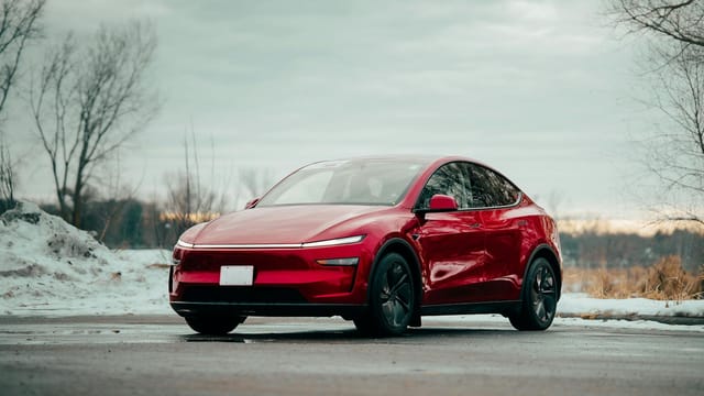 Red electric car parked outdoors, showcasing sleek design amidst winter scenery.