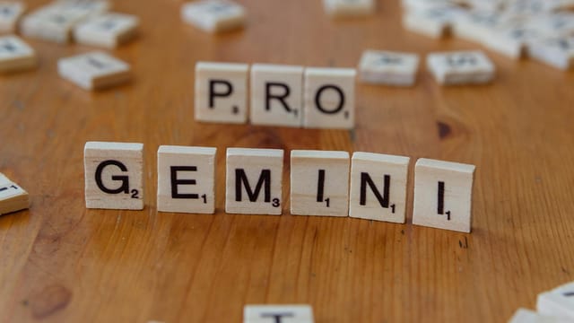Scrabble tiles arranged to spell 'PRO GEMINI' on a wooden table, ideal for creativity themes.