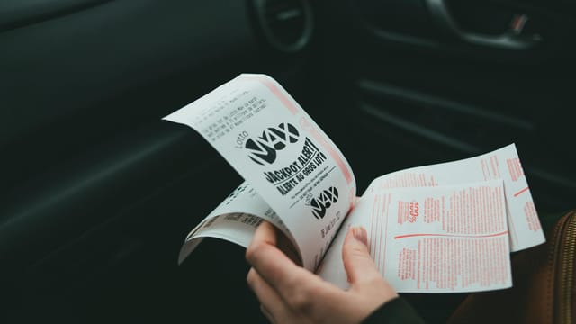 Close-up of hands holding Lotto Max papers inside a car, symbolizing luck and chance.