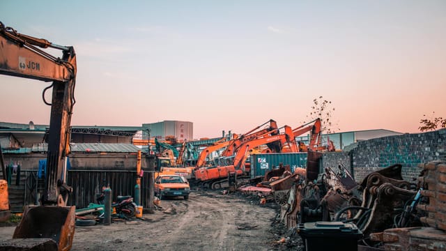 A busy construction site with industrial machinery at sunset, showcasing excavators and a vibrant sky.