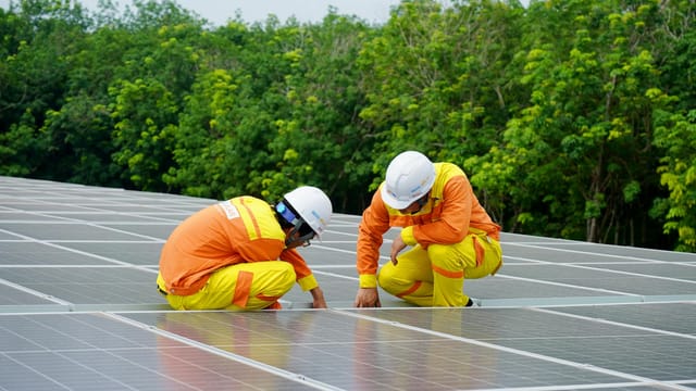 Workers installing photovoltaic solar panels on a sunny day, promoting renewable energy.