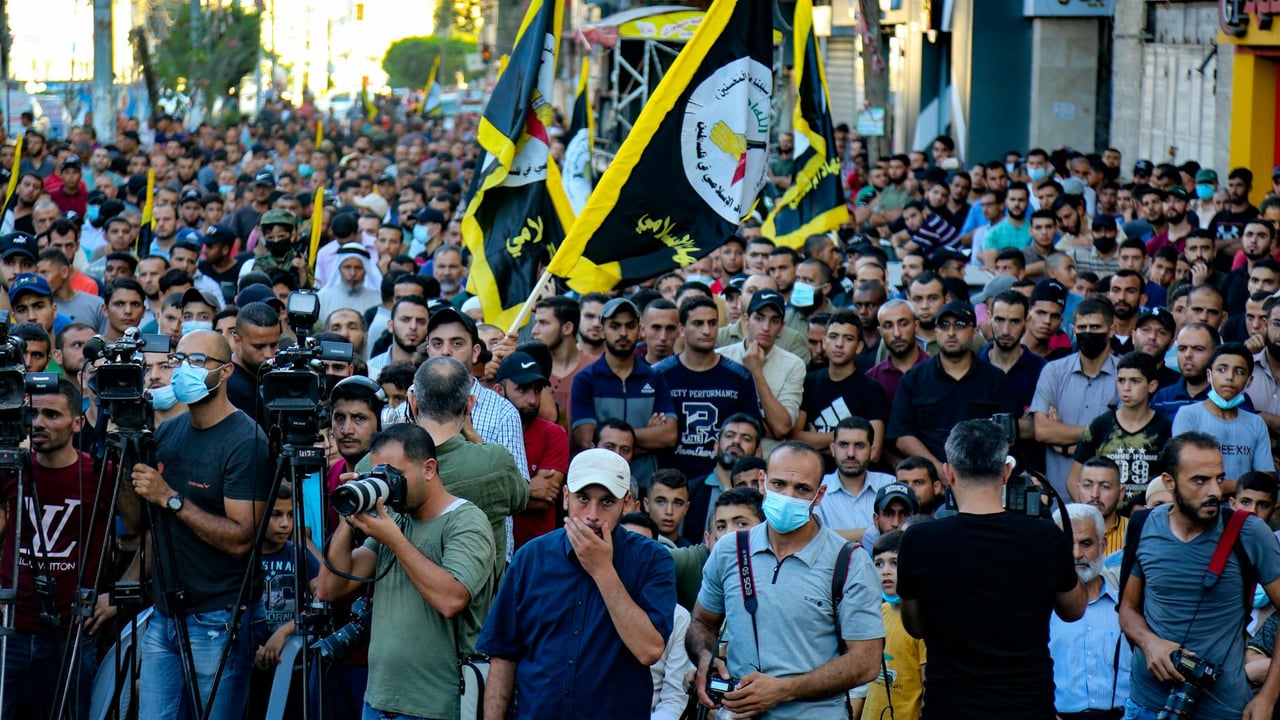 A vibrant demonstration with flags and photographers on a street in Gaza.