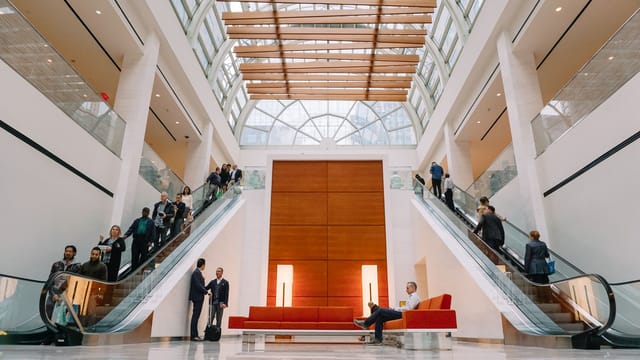 Group of people on benches and elevators in bright spacious hall of shopping center decorated in white colors