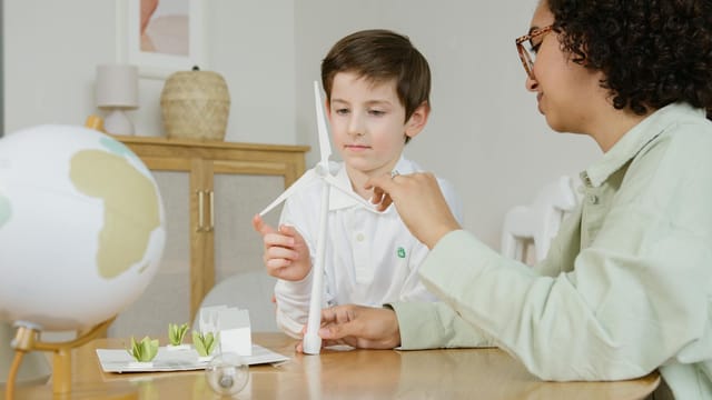 A boy and teacher exploring a wind turbine model, promoting environmental education.