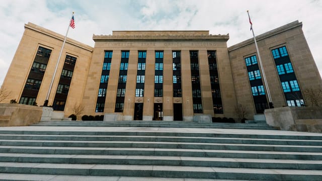 From below of Federal Reserve building exterior against USA flags and staircase under cloudy sky in town