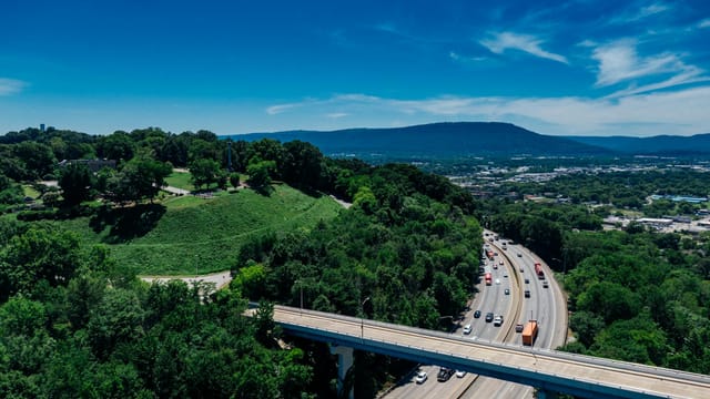 Aerial view of Chattanooga's lush greenery, highway, and distant mountains on a sunny day.