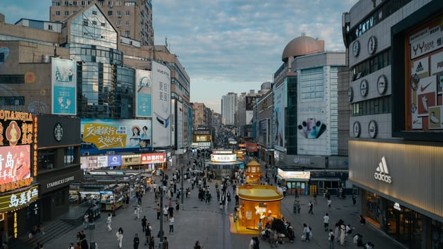High-angle view of a crowded urban shopping district with illuminated advertisements and diverse architecture.