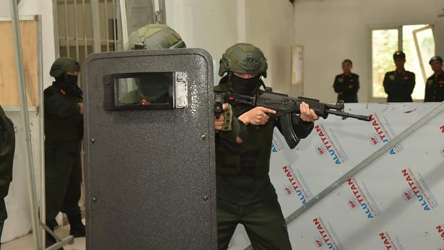 Armed security personnel conducting a tactical training exercise indoors with shields and weapons.