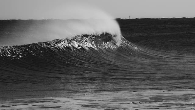 A dramatic black and white photo capturing a powerful ocean wave crashing, with a moody and dramatic feel.