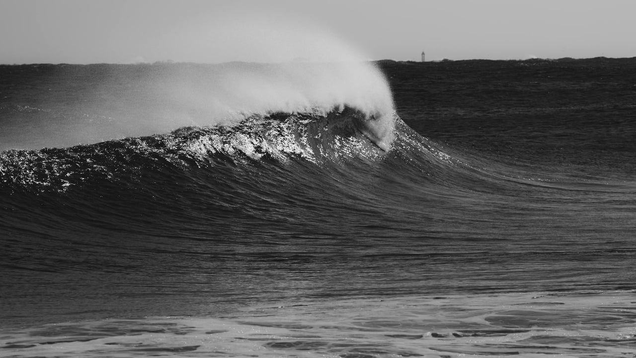 A dramatic black and white photo capturing a powerful ocean wave crashing, with a moody and dramatic feel.