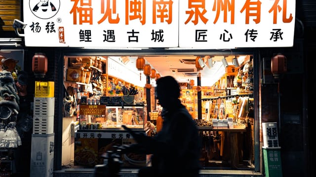 Silhouette of a person passing a vibrant night market shop in Quanzhou, China.