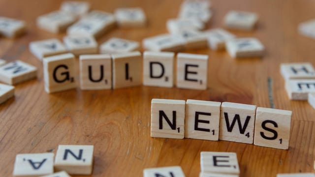 Close-up of Scrabble tiles spelling 'Guide' and 'News' on a wooden surface.