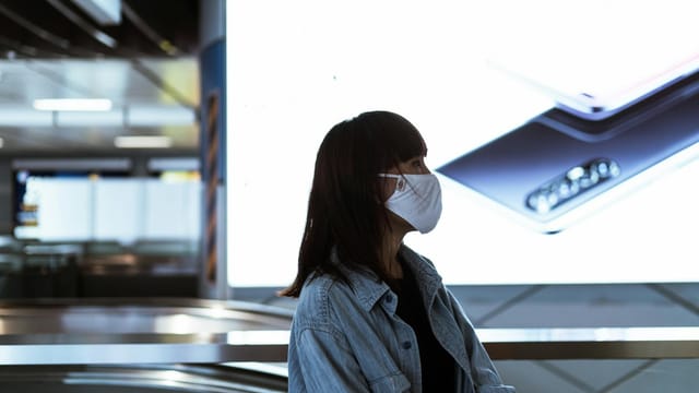 Profile of a woman in a mask, indoors with digital display, city life.