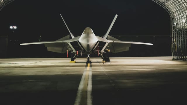 A Lockheed Martin F-22 Raptor jet parked symmetrically in a hangar at night.