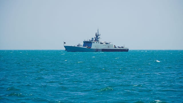 A navy patrol ship sailing on clear tropical waters under a bright sky.