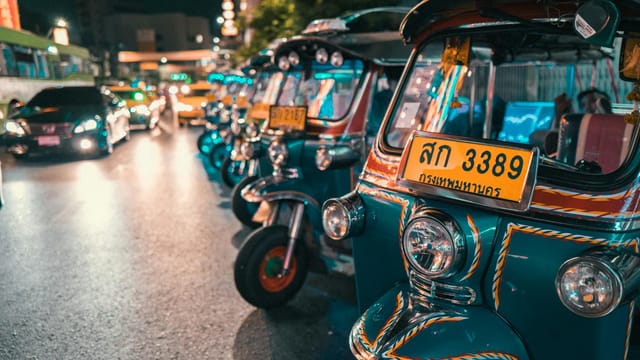 Vibrant row of tuk-tuks at night, illuminating the busy Thai city streets.