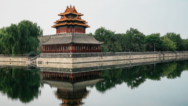A scenic view of the iconic corner tower of the Forbidden City with its reflection in the moat.