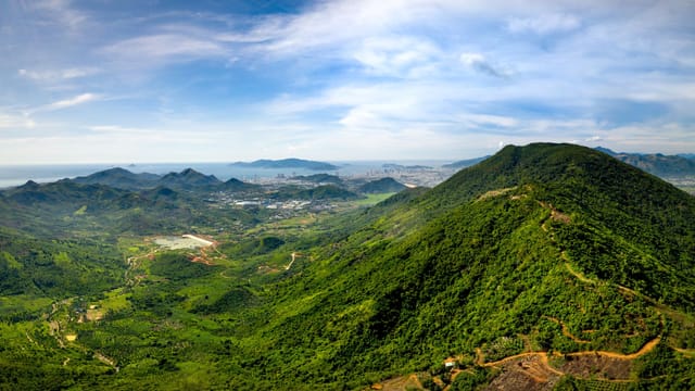 Breathtaking aerial view of lush mountain range and cityscape under a bright blue sky.