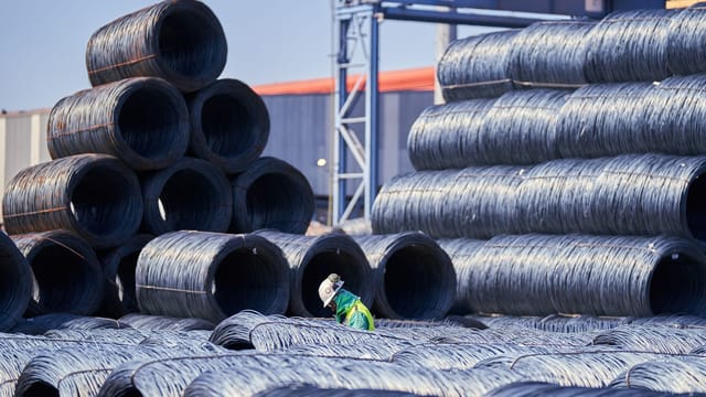 A solitary worker in protective gear inspects stacked steel coils at an industrial site.