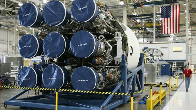Unfinished details of rocket engines under construction placed on metal platform during assembly at space factory with hanging US flag on background
