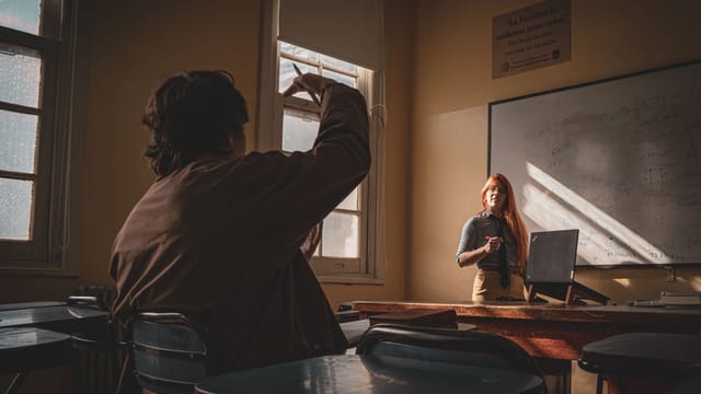 A teacher interacts with a student in a sunlit classroom setting, fostering learning and engagement.