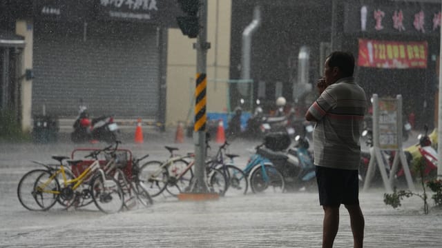 A man stands smoking under shelter, watching the rain pouring on a city street in Pingtung County, Taiwan.