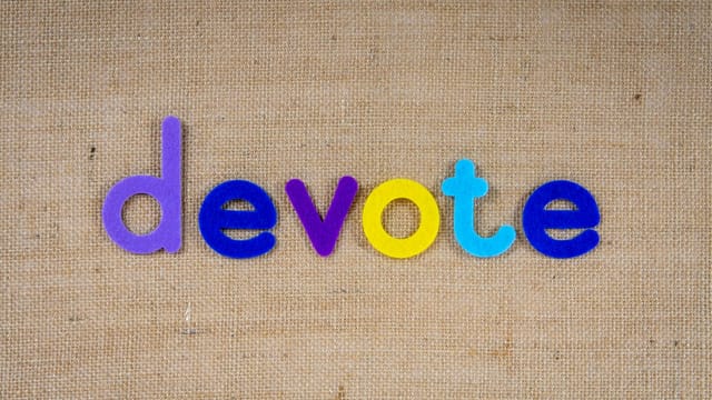 Colorful letters forming the word 'devote' on burlap fabric background.