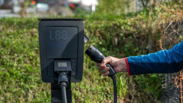 An outdoor electric car charging station with a hand holding a charging cable.