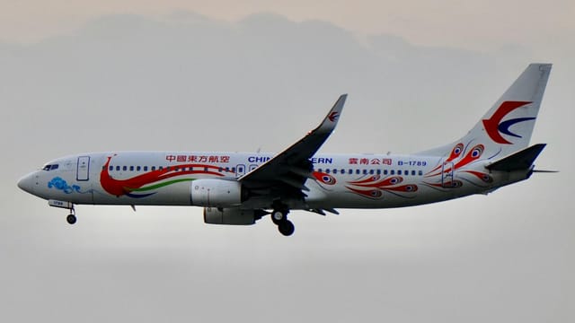China Eastern Airlines plane with vibrant design in flight against a cloudy sky.