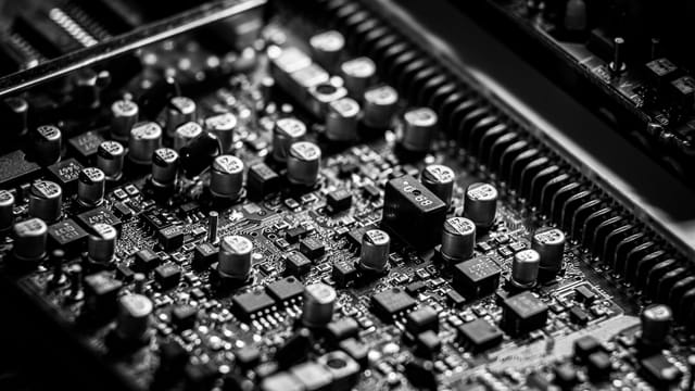 Detailed black and white close-up of an electronic circuit board, highlighting capacitors and microchips.