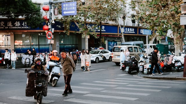 Street life in Nanjing, China with people, scooters, and autumn foliage on a busy corner.